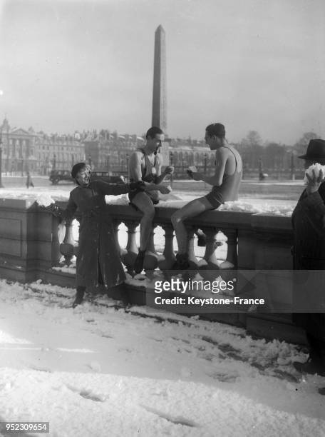 Deux hommes en tenue très légère sont assis sur un parapet et rient avec une femme en manteau sur la place de la Concorde recouverte de neige circa...