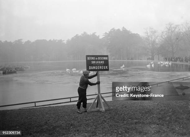 Un homme installe un panneau 'dangereux' référant à la surface gelée du lac au Bois de Boulogne en 1935 à Paris, France.