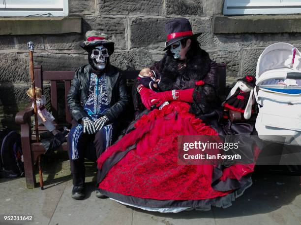 Couple dressed in Goth clothing carrying baby dolls sit on a bench during Whitby Gothic Weekend on April 28, 2018 in Whitby, England. The Whitby Goth...