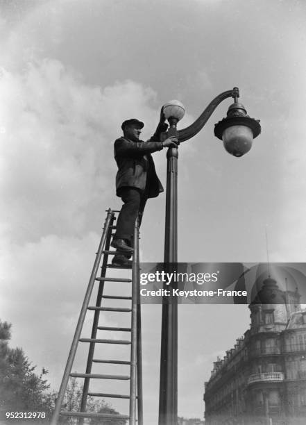 Un ouvrier installe la cellule photoélectrique sur un lampadaire à Paris, France en mai 1933.