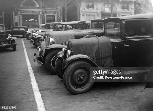 Sur un parking, les radiateurs des automibiles sont protégés par une couverture contre le froid, à Paris, France le 9 janvier 1935.