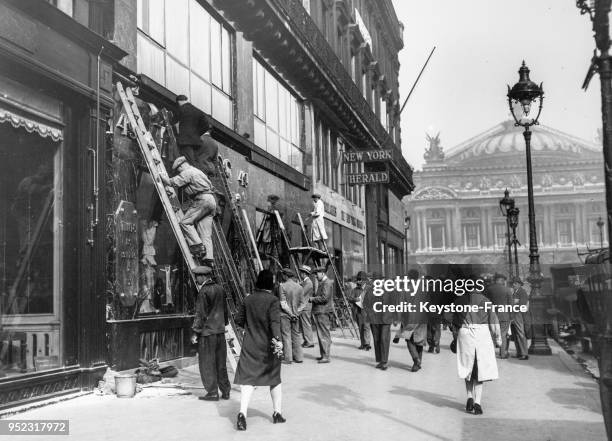 Des laveurs sur des échelles nettoient les vitrines d'un magasin de l'Avenue de l'Opéra en septembre 1929 à Paris, France.