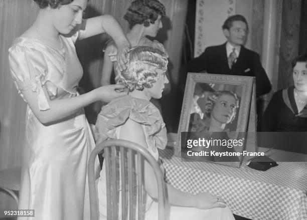 Une coiffeuse fait à sa cliente une coiffure 1900 pour un défilé, à Paris, France en 1934.
