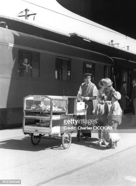 Un vendeur de sandwiches rend la monnaie a une cliente sur le quai de la gare, en 1959 a Paris, France.