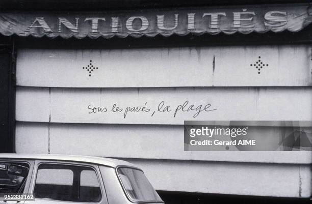 Graffiti ?sous les pavés, la plage? sur le store d'une boutique d'antiquités à Paris, en mai 1968, France.