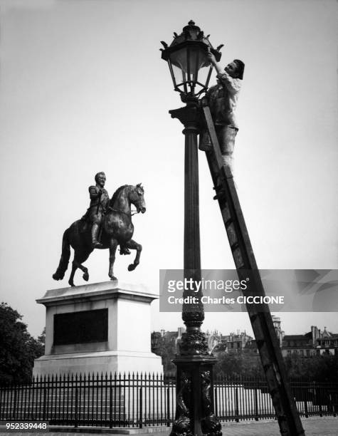 Employé de la municipalité de Paris repeignant un lampadaire de la place Dauphine, devant la statue équestre d'Henri IV, France.