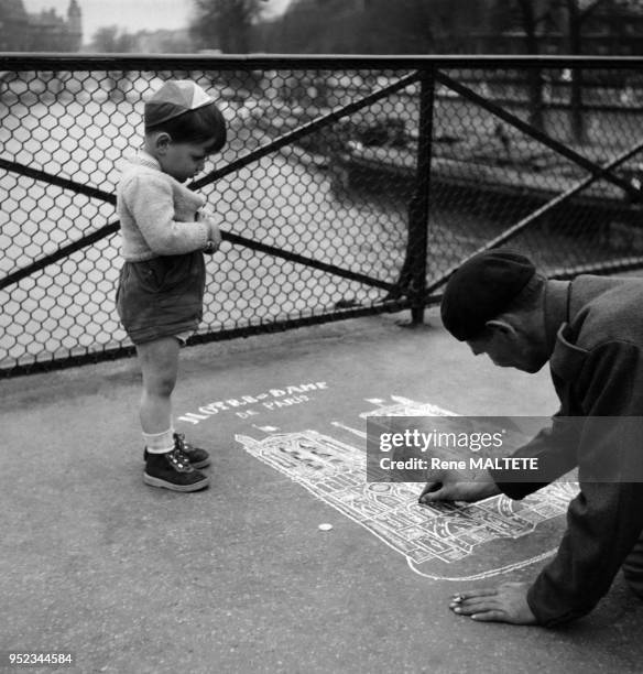 Enfant observant un dessinateur reproduisant la cathédrale Notre- Dame à la craie sur le trottoir à Paris, France.