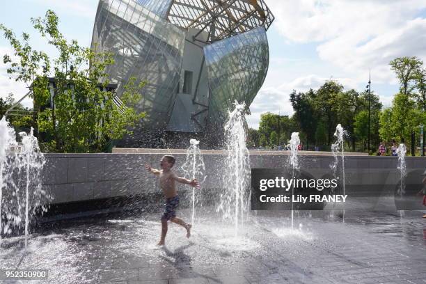 Jardin d'acclimatation, enfant jouant sous les jets d'eau, près de la fondation Louis Vuitton., 21 juillet 2015, Paris, France.