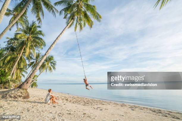 coppia che gioca sulla spiaggia, corda oscillante sulla palma nell'isola tropicale asia - altalena di corda foto e immagini stock