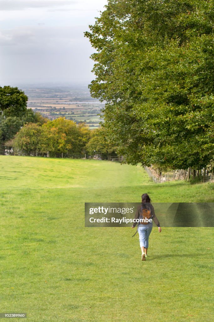 Unbeschwerte junge Frau schreiten durch die Cotswold-Landschaft auf dem Weg hinunter Broadway Stadtzentrum in Cotswolds