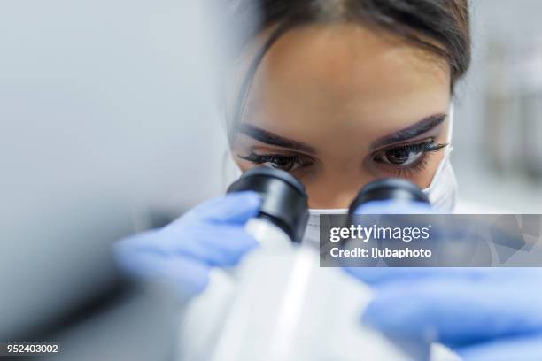 cerca del joven científico mirando a través de un microscopio en un laboratorio - exactitud fotografías e imágenes de stock