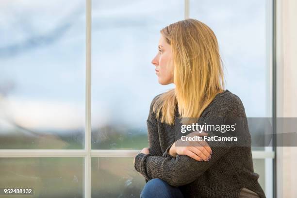 young woman looks out the window pensively - woman suicide stock pictures, royalty-free photos & images