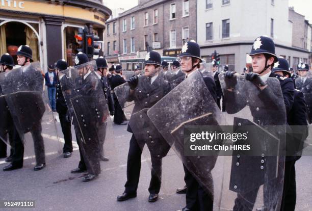 Des policiers britanniques en uniformes et abrités derrière des boucliers dans la rue lors des émeutes raciales de Brixton en avril 1981 à Londres,...