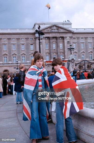 Deux jeunes gens se sont enveloppés dans le drapeau anglais devant le Palais de Buckingham, circa 1970 à Londres, Royaume-Uni.