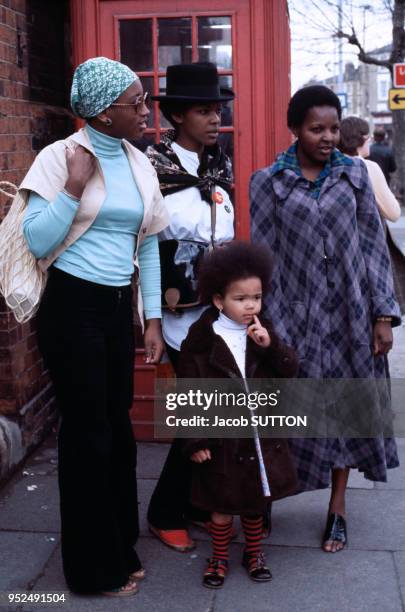 Des femmes noires et une petite fille près d'une cabine téléphonique typiquement britannique, circa 1970 à Londres, Royaume-Uni.