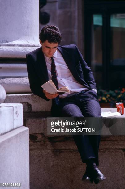 Un jeune homme en costume cravate lit un roman pendant sa pause.