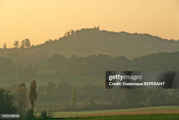 Paysage du Haut Agenais, le village de Monflanquin, vue lointaine a contre-jour de la colline de Monflanquin au lever du soleil, brume matinale et...