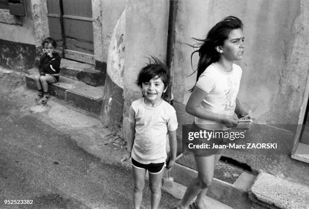 Un petit garçon assis sur une marche d'escalier et deux autres enfants marchant dans la rue, scène de vie quotidienne dans le quartier de la Roquette...