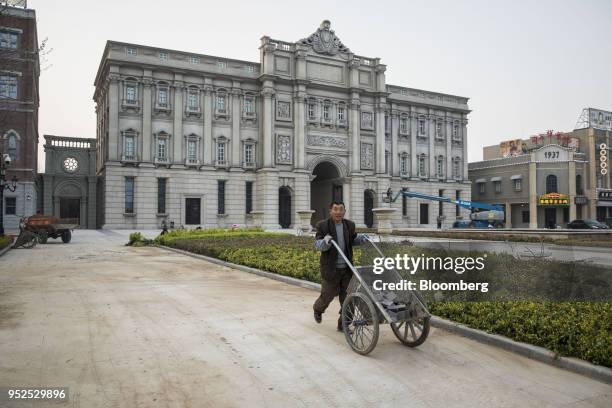 Worker pushes a cart in front of a film set resembling Shanghai architecture from the 1920s at a backlot of the Dalian Wanda Group Co. Oriental Movie...
