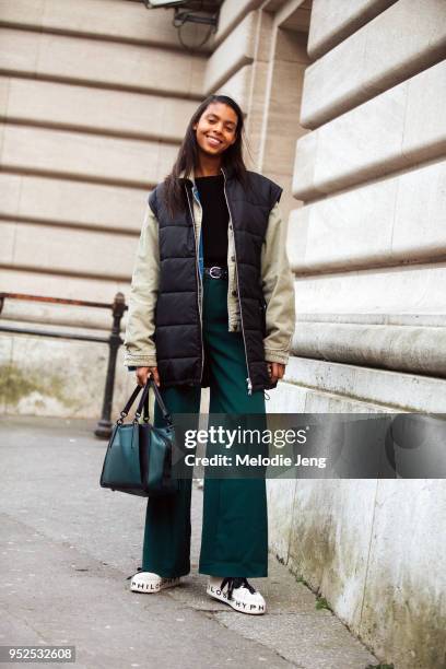 Model Alyssa Traore wears a black down vest over a cream corduroy denim jacket, a black shirt, wide-leg green trousers, a green Coach bag, and...