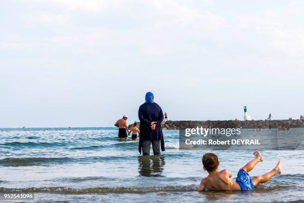 Une femme musulmane habillée, les pieds dans l'eau, regarde sa famille se baigner dans la mer, 11 juillet 2016 Carnon, Hérault, France.