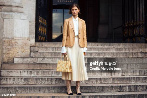 Model Giedre Dukauskaite wears a tan leather blazer, white skirt, a beige pleated skirt, a yellow Celine python medium clasp tote, and Chanel glitter...