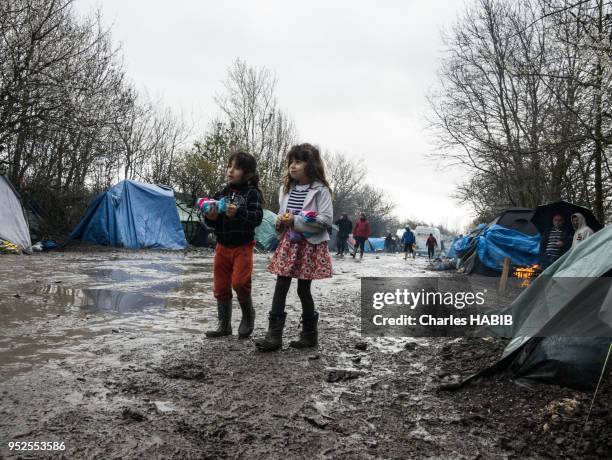 Deux fillettes avec des bottes marchant dans une rue boueuse, camp de réfugiés, le 16 février 2016, Dunkerque, France.