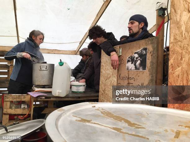 Une jeune femme bénévole servant une boisson chaude, un homme tenant un panneau 'Kurdistan downtown Nord 4 ever', camp de réfugiés, le 16 février...