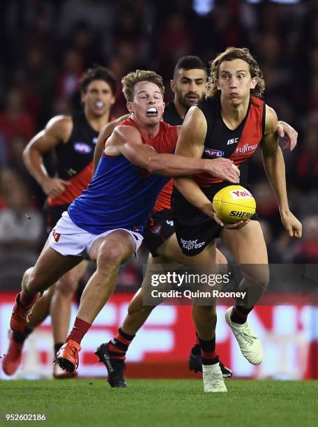 Kobe Mutch of the Bombers handballs whilst being tackled by Mitch Hannan of the Demons during the round 6 AFL match between the Essendon Bombers and...