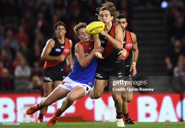 Kobe Mutch of the Bombers handballs whilst being tackled by Mitch Hannan of the Demons during the round 6 AFL match between the Essendon Bombers and...