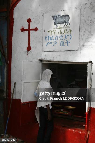 Shop of a Christian butcher in Ethiopia. On the outside wall can be seen a picture of a bull, and a cross. A young woman is entering the store, 2009...