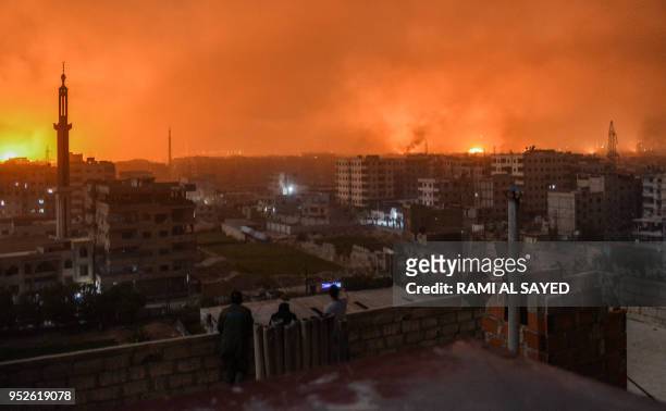 People stand on a roof to observe explosions in the skyline of a southern district of the Syrian capital Damascus, during regime strikes targeting...