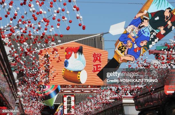 Grande planche en bois avec un coq dessiné dessus et divers objets qui portent chance installés au-dessus de la rue commerçante Asakusa Nakamise...