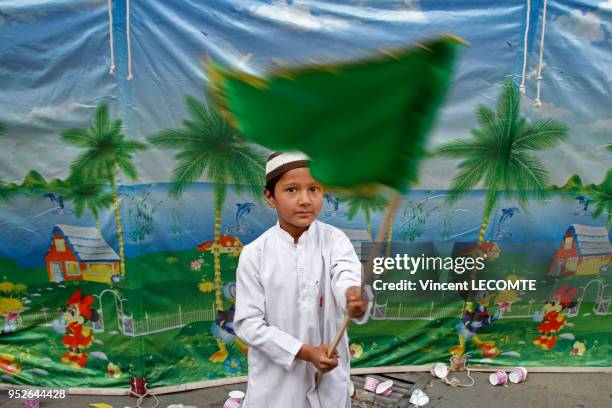 Jeune garçon indien musulman agitant un drapeau aux couleurs de l?islam lors d?une manifestation pro-islamique, photographié dans une rue décorée...