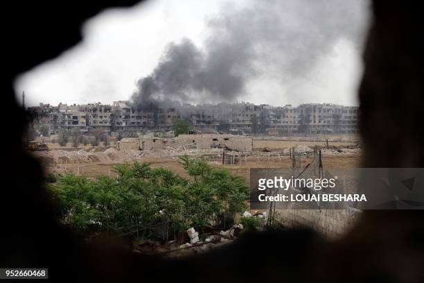 Picture taken on April 29 during a government guided tour in Damascus' southern al-Qadam neighbourhood, shows smoke rising from buildings in Yarmuk,...