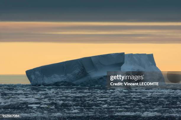 Un iceberg dérive lentement à l?horizon sur l'Océan Glacial Antarctique, au large de la Terre Adélie, en Antarctique, tandis que le soleil austral se...