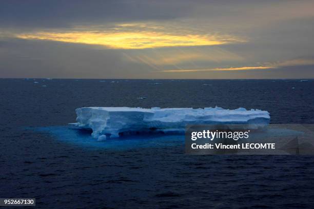 Un iceberg dérive lentement à l?horizon sur l'Océan Glacial Antarctique, au large de la Terre Adélie, en Antarctique, tandis que le soleil austral se...