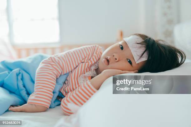 asian sick little girl lying in bed with a high fever - forehead stock-fotos und bilder