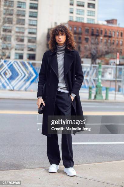 Model Ana Arto wears a Deveaux coat, gray top, black trouses, and white sneakers on February 12, 2018 in New York City.