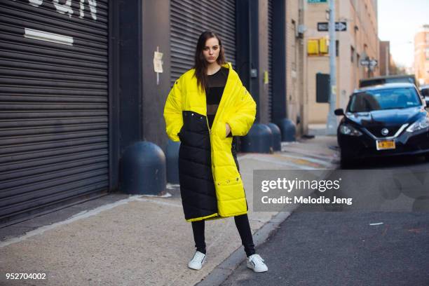 Model Emm Arruda wears a black yellow long down puffer parka with a black sheer top and white sneakers February 12, 2018 in New York City.