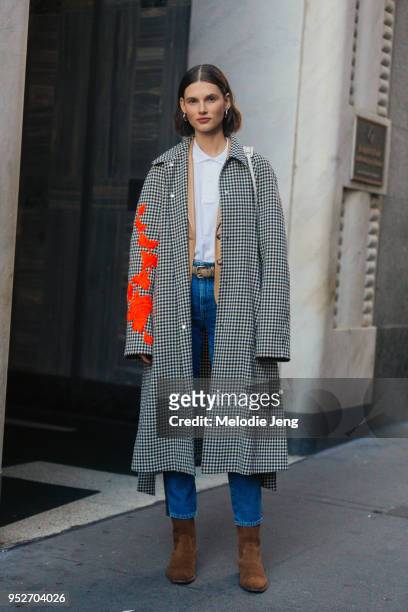 Model Giedre Dukauskaite wears a black and white gingham coat with orange floral embellishment, a white top, blue jeans, and brown suede Saint...