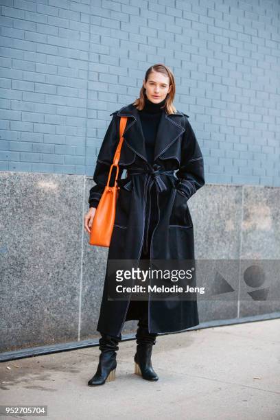 Model Sanne Vloet wears a blue trench coat with a belt, an orange purse, and black boots on February 8, 2018 in New York City.