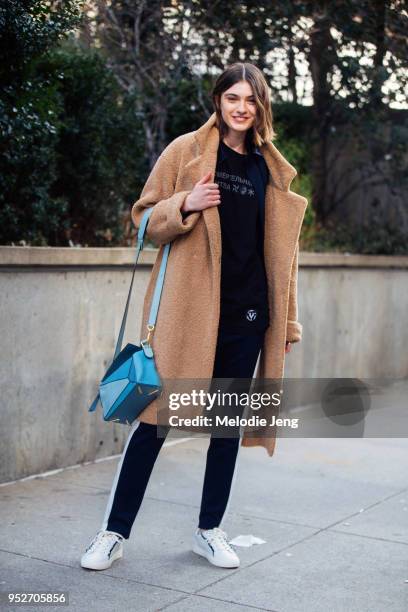 Model Milena Litvinovskaya wears a brown teddy bear coat, blue Loewe puzzle bag, a black shirt with russian text, Tory Sport black joggers, Tory...