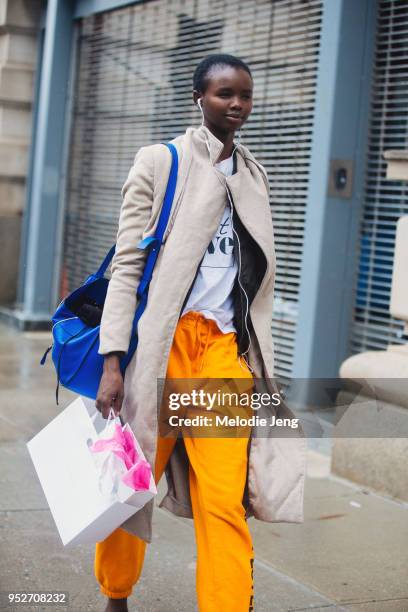 Model Akiima wears a tan coat, white shirt, and yellow pants on February 11, 2018 in New York City.