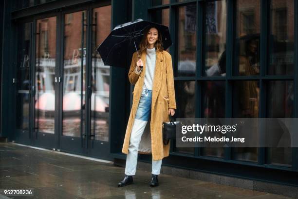 Model Alana Zimmer holds an umbrella and wears a Suzanne Rae corduroy amber coat, black Elleme bag, B SIDES jeans, and black booties after the Tibi...