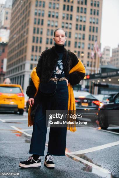 Model Julia Nicole Meyer wears oversized glasses, an orange scarf off her shoulders, a black fringe purse, jeans, and black chunky sneakers on...