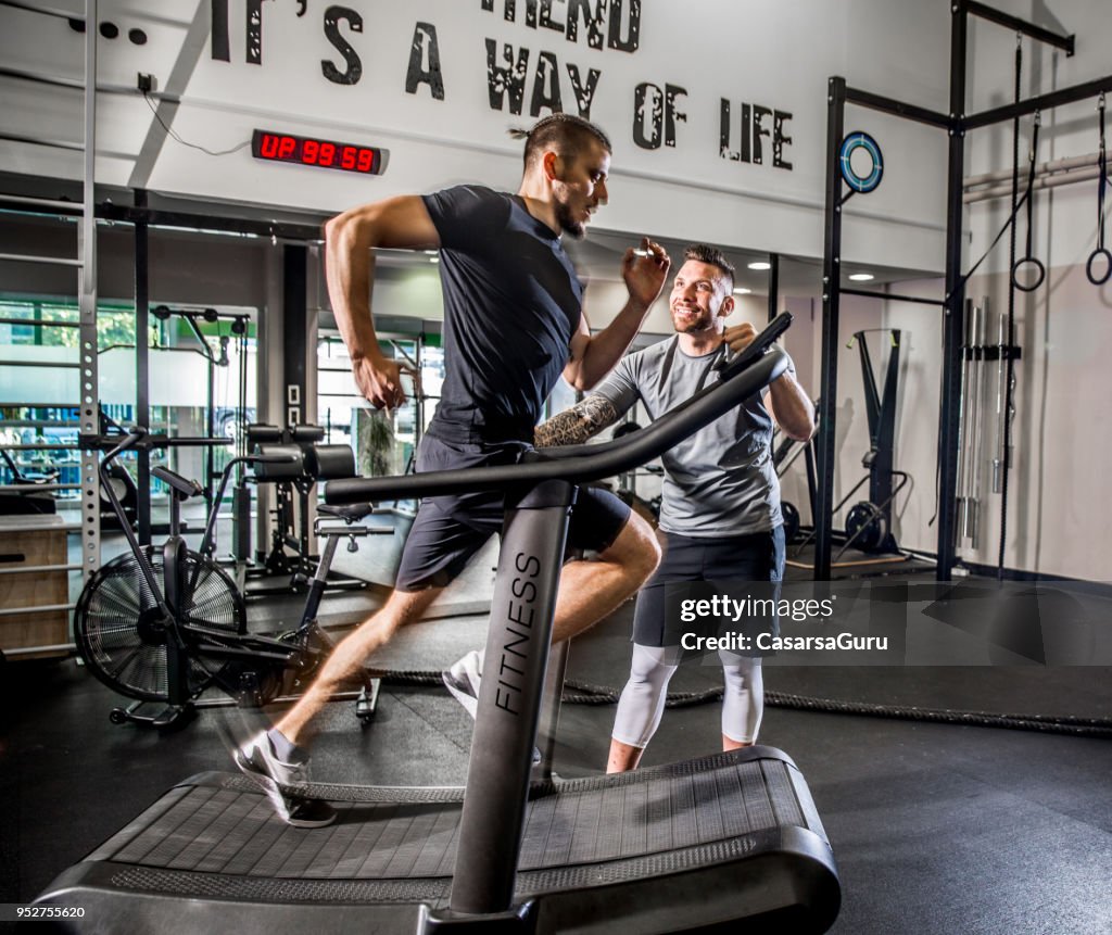 Young Man Running on Treadmill while Fitness Instructor Motivates Him