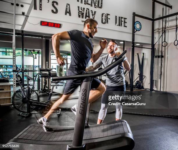 young man running on treadmill while fitness instructor motivates him - running on treadmill stock pictures, royalty-free photos & images