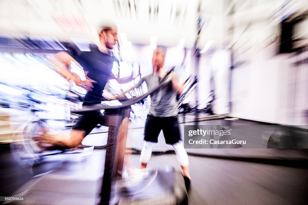 Jovem homem correndo na esteira enquanto Fitness instrutor motiva-lo