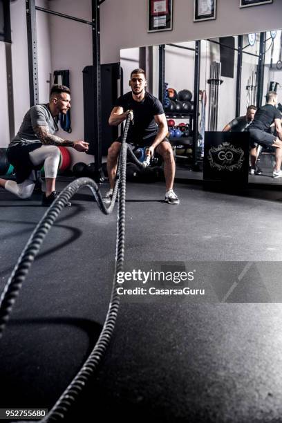 ung vuxen man svängande linor medan fitnessinstruktör motiverar honom - personlig tränare bildbanksfoton och bilder